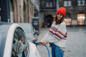Frau mit roter Wollmütze steckt Ladekabel in Elektrofahrzeug