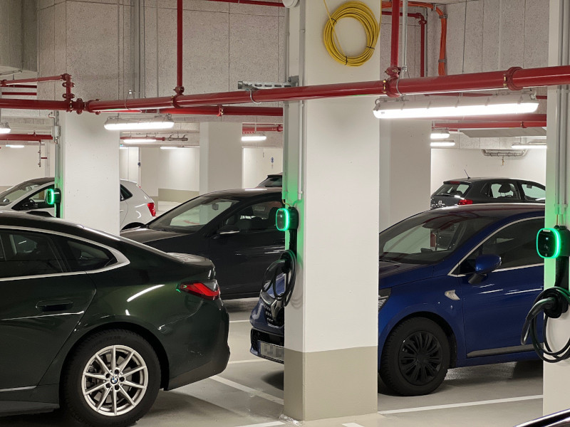 Tiefgarage mit mehreren parkenden Autos, an drei nebeneinander stehenden Betonpfeilern hängt jeweils eine grün leuchtende LADEmini Wallbox